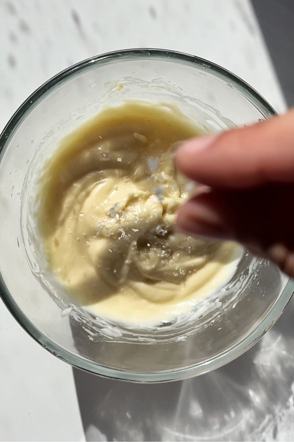 Adding salt into homemade kewpie mayonnaise in a glass bowl.
