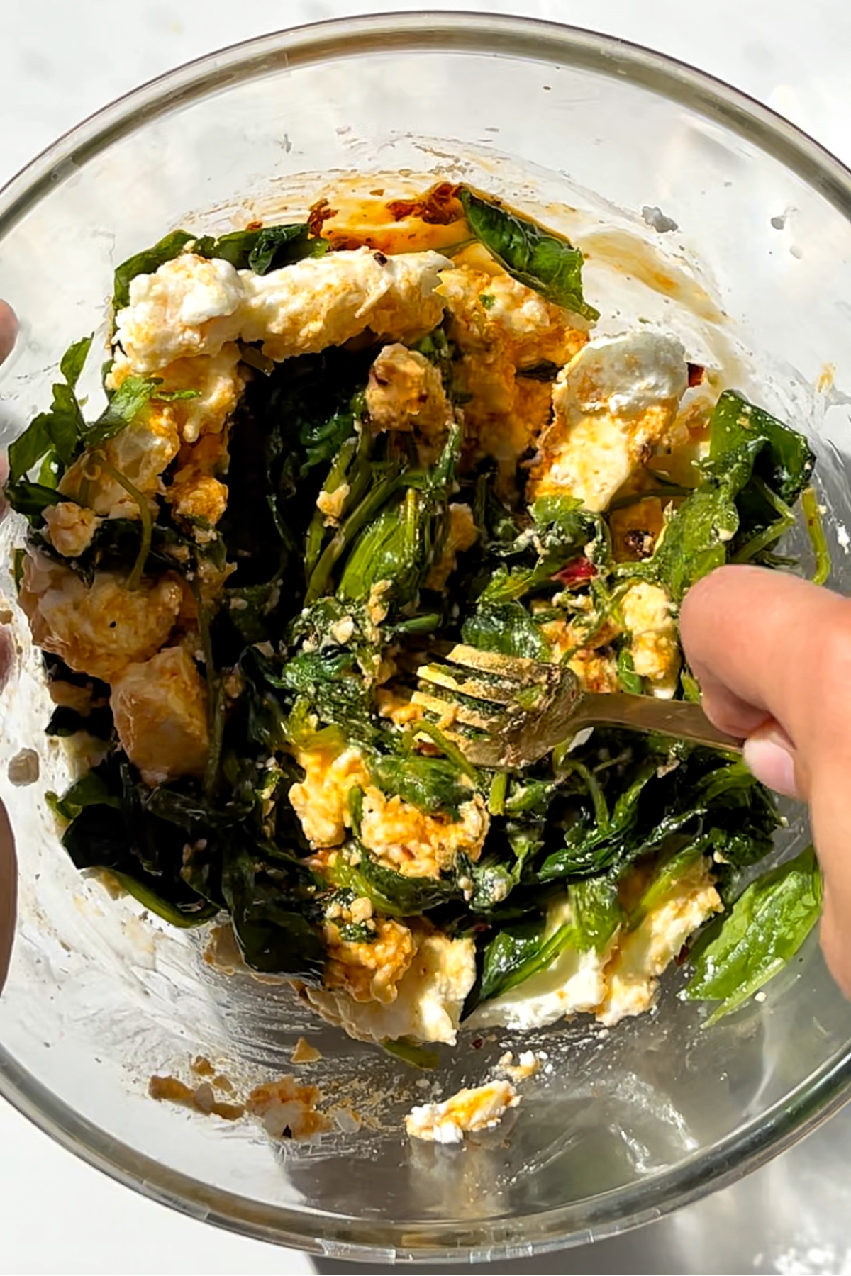 Combining feta, spinach, egg, and chilli oil in a glass bowl.