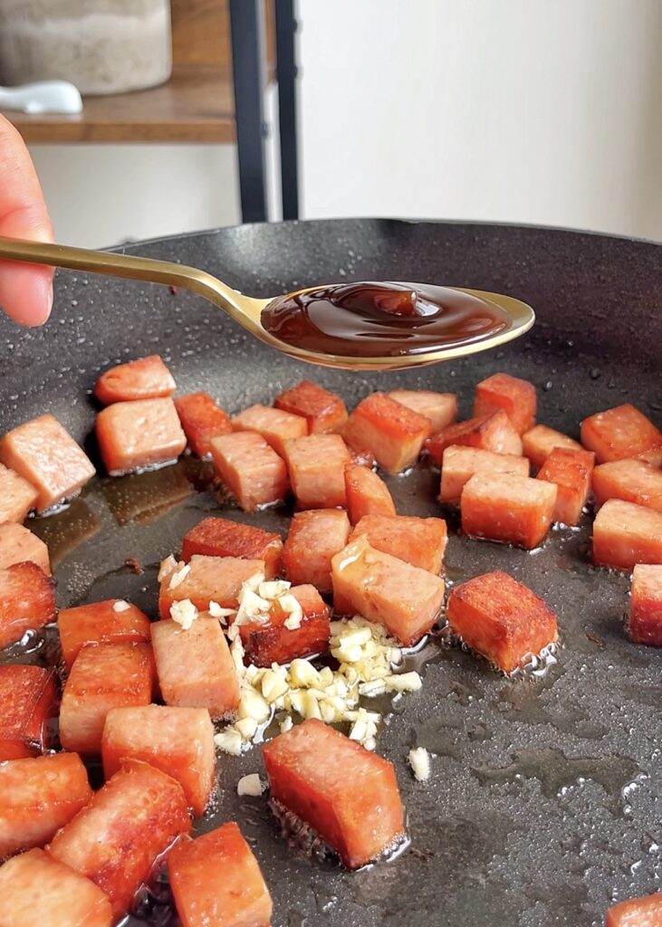 Adding seasonings into a frying pan filled with fried spam