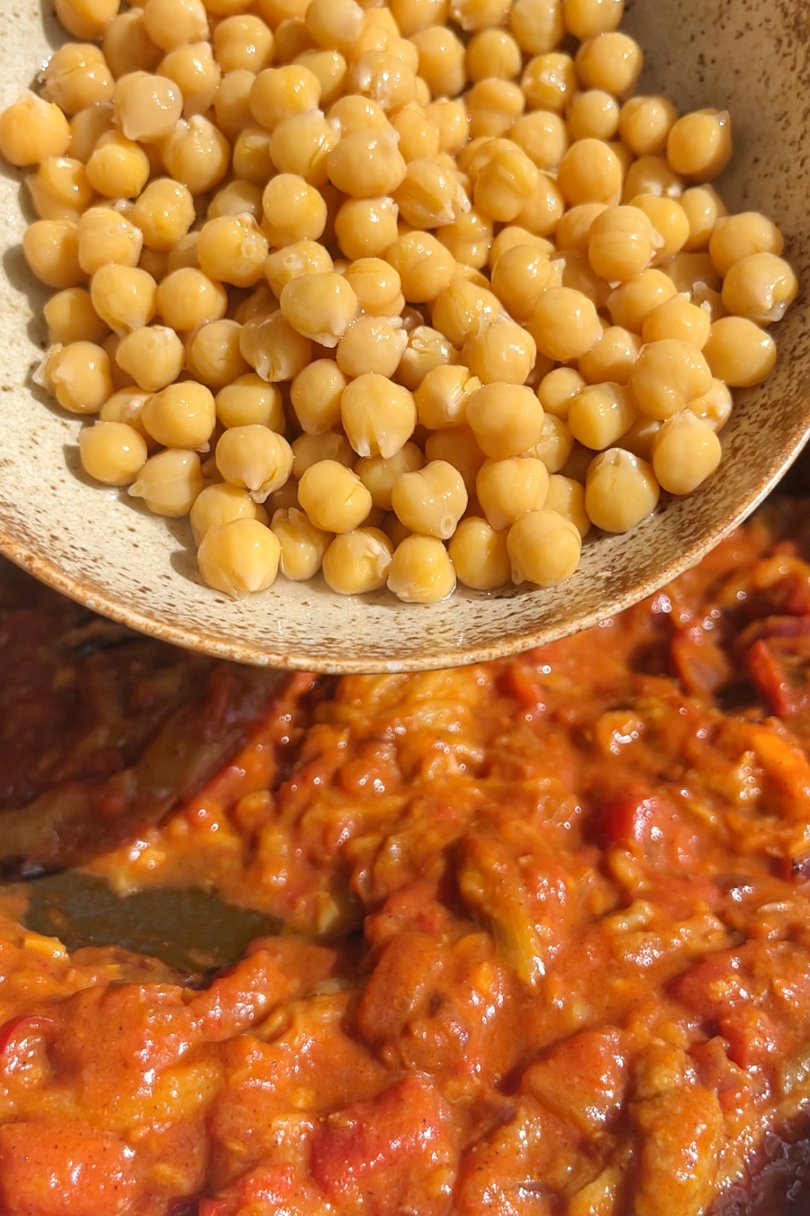 Pouring in chickpeas into a curry.