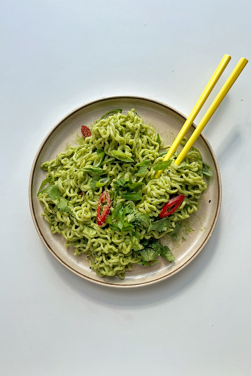 Plate of green tahini miso noodles with yellow chopsticks.
