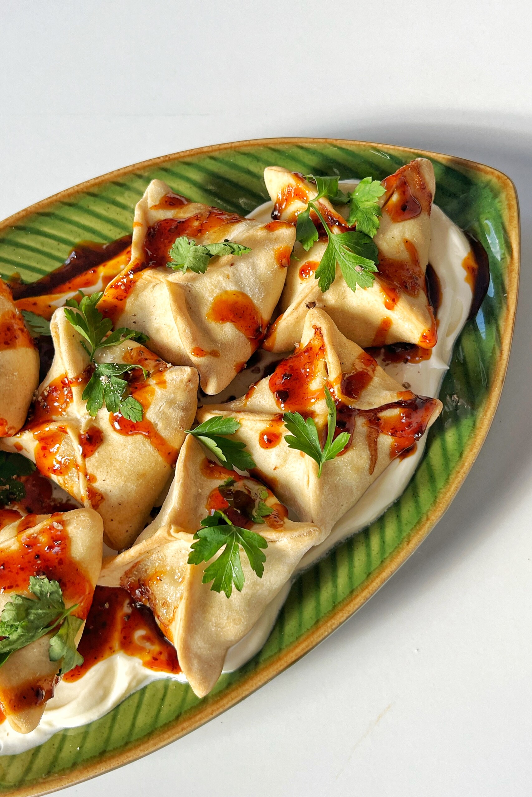 Close up of dumplings in a honey harissa dressing on green plate.