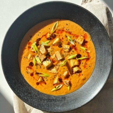 Black bowl with tofu tomato soup in it.