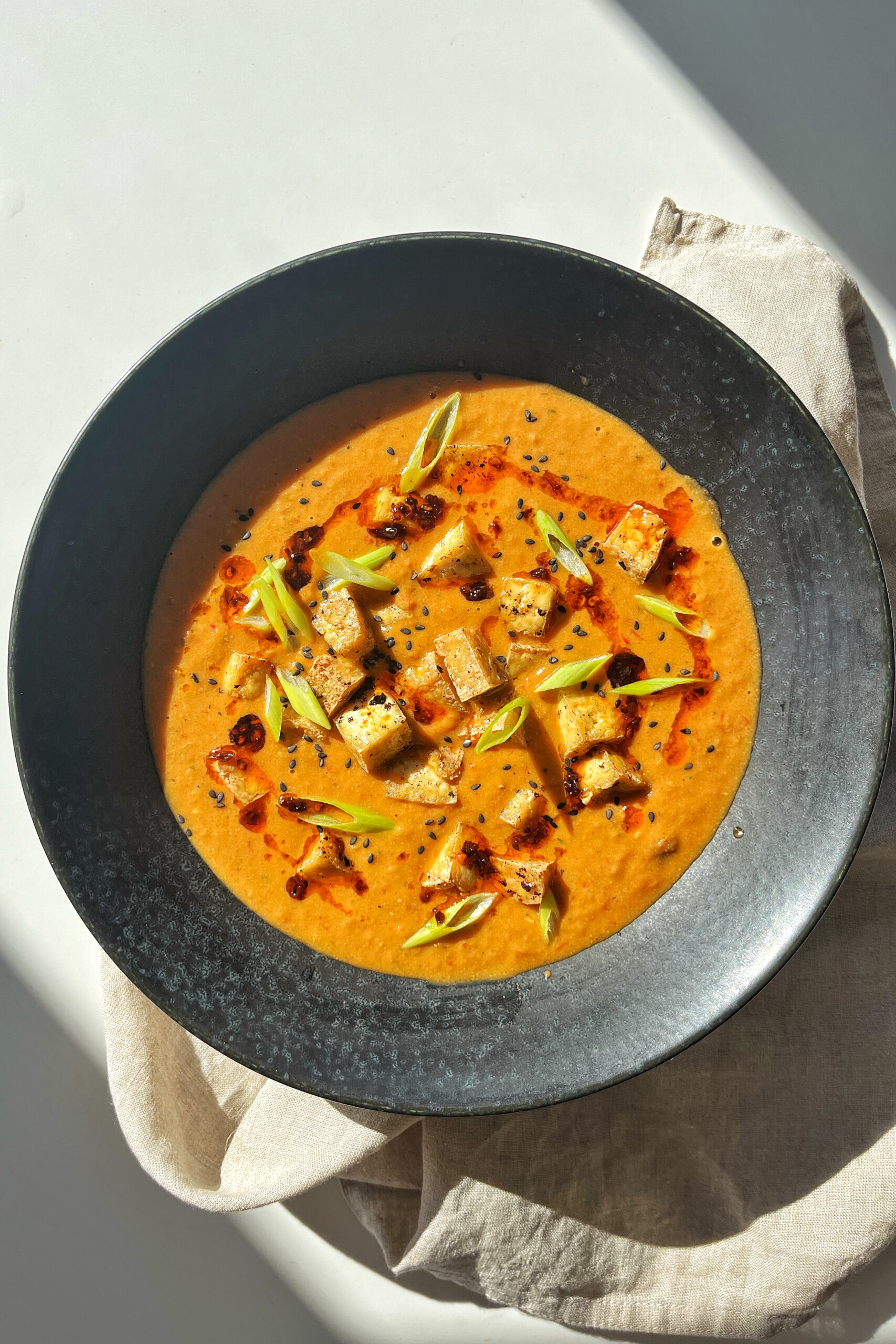 Black bowl with tofu tomato soup in it. 