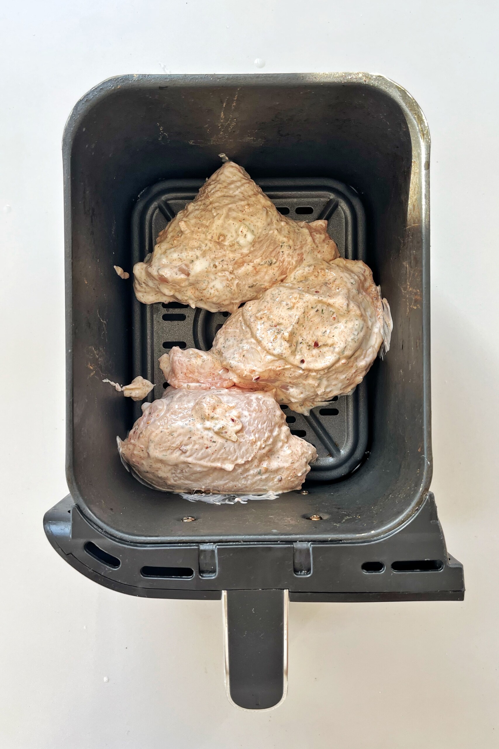 Marinated chicken placed in the air fryer compartment.