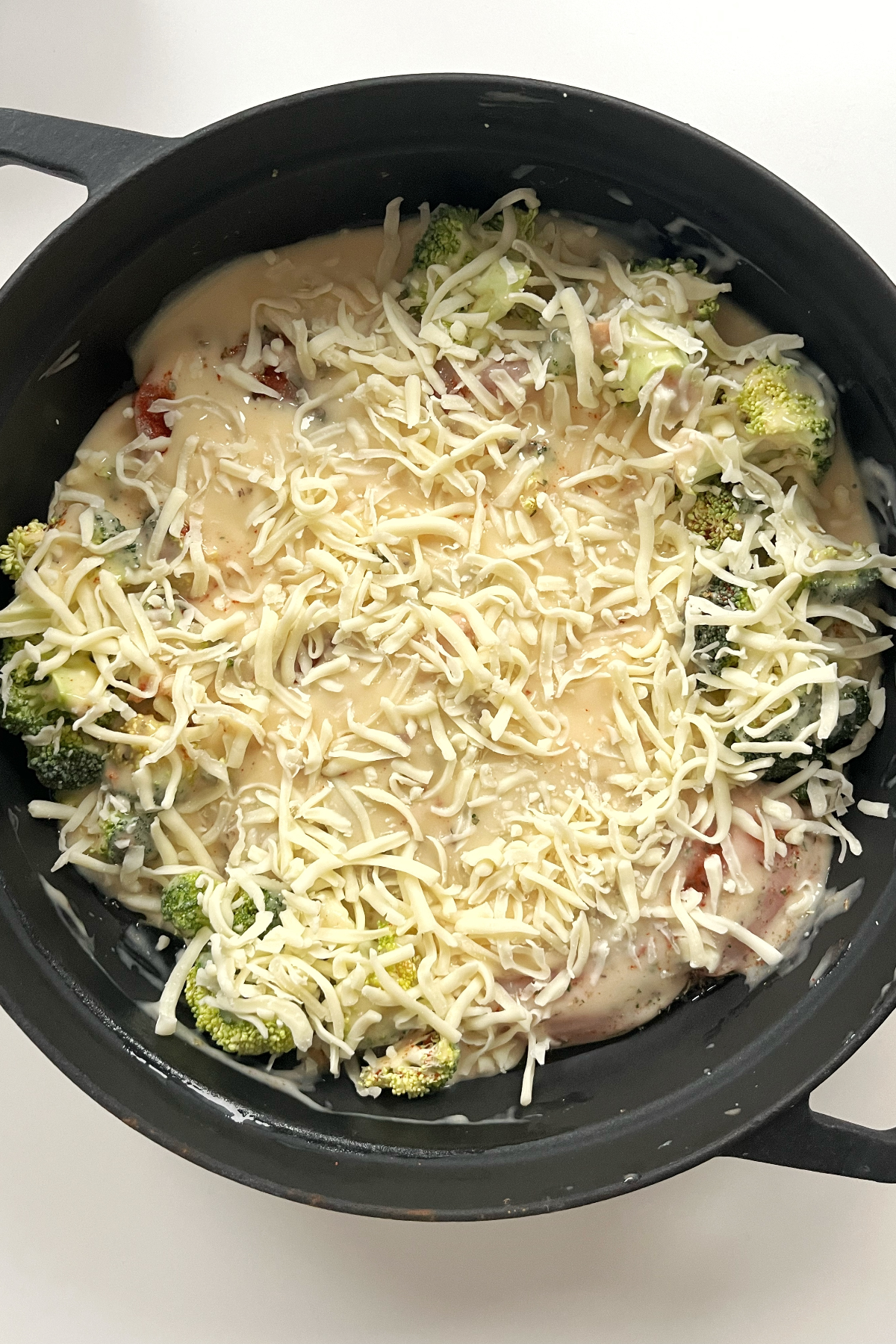 Black casserole dish with chicken, broccoli, cream of chicken soup, and cheese.