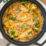 Cheesy baked chicken in a black pan topped with parsley.