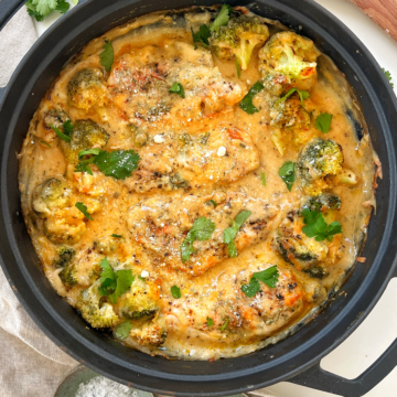Cheesy baked chicken in a black pan topped with parsley.