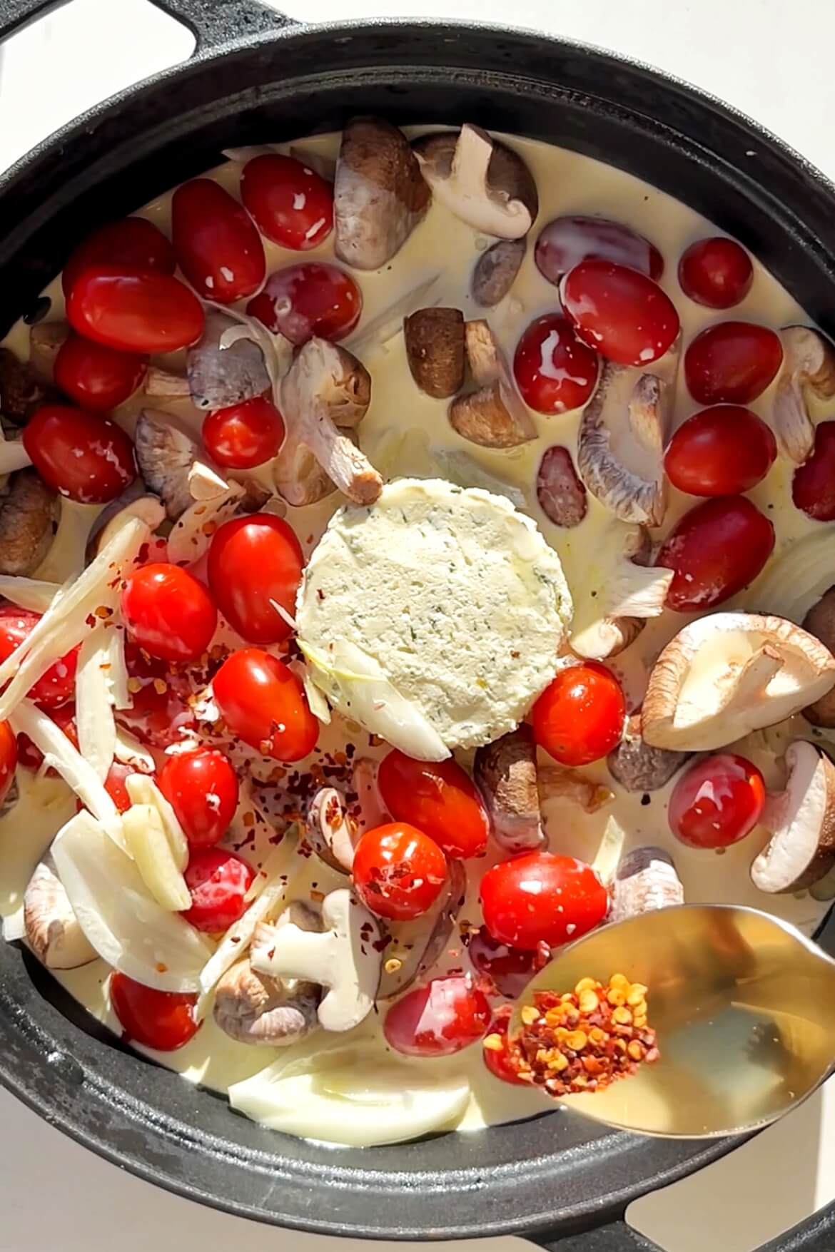 Black pan with Boursin, tomatoes, garlic, mushrooms, and chilli flakes.