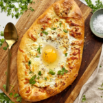 Cheese boat pie with egg in the middle on a brown wooden board.