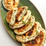 Chive pockets on a green plate with one chive pie opened in half.