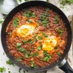 Sardines and eggs in a black pan with sprinkled parsley.