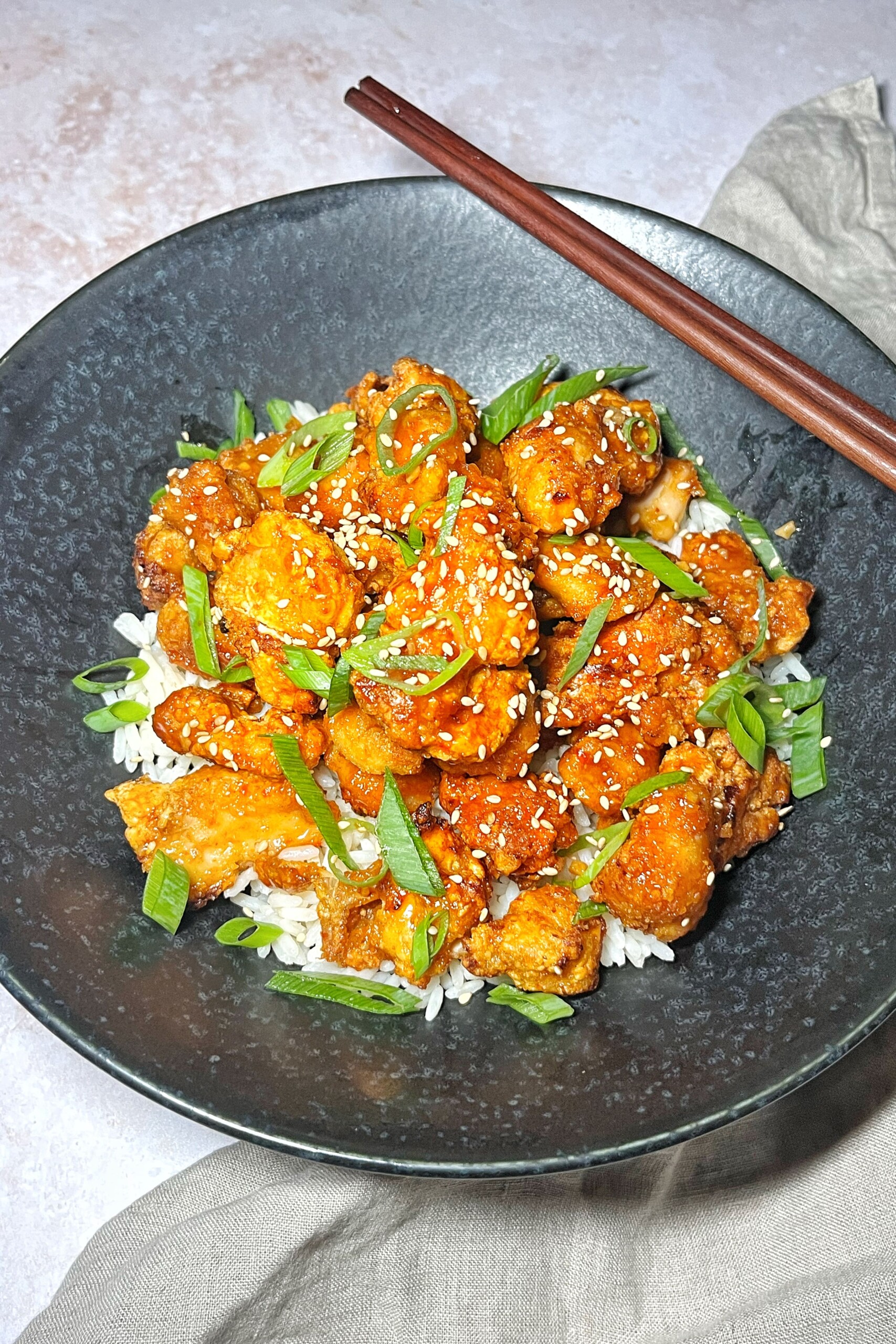 Volcano chicken in black bowl with rice and chopsticks.