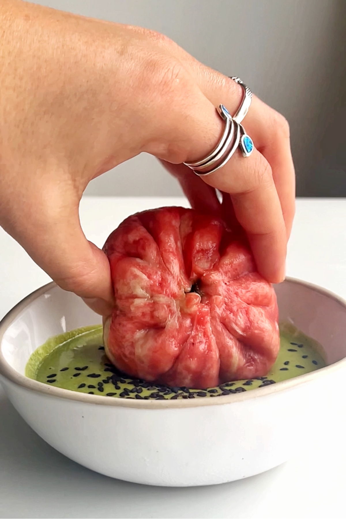 Dipping the grinch dumplings into a green tahini sauce in white bowl.