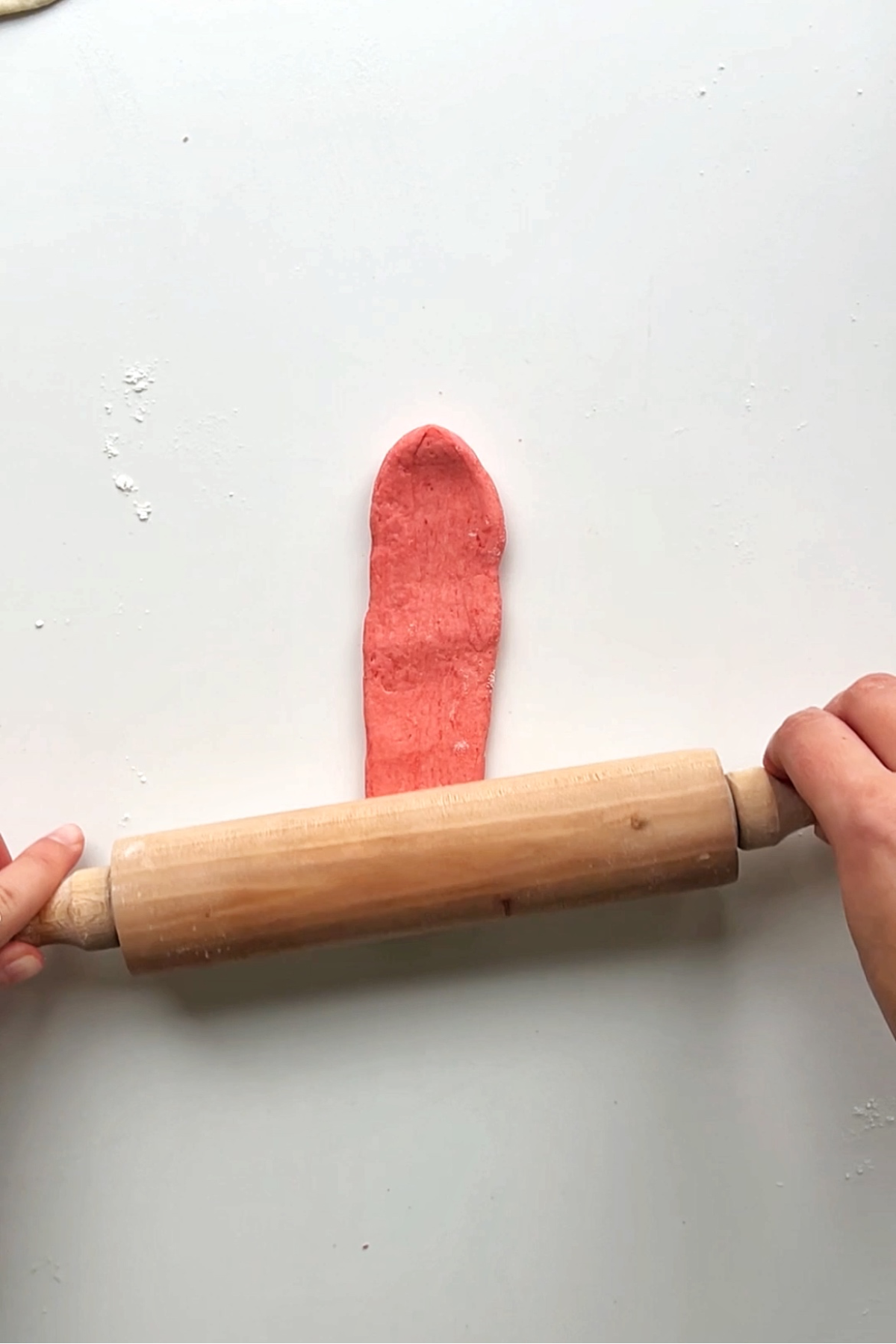 Rolling out pink piece of dough using rolling pin.