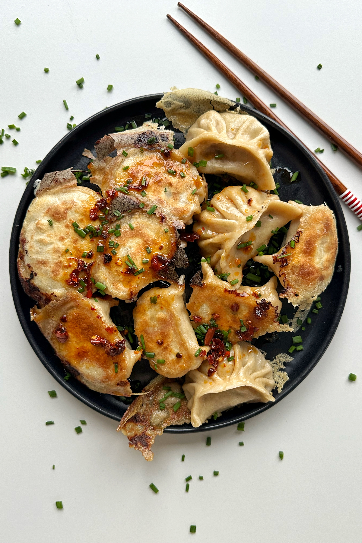 Dumplings scattered on a black plate with chopsticks and chives. 