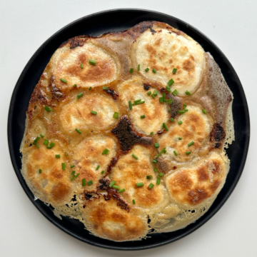 Crispy skirt dumplings on black plate topped with chives.