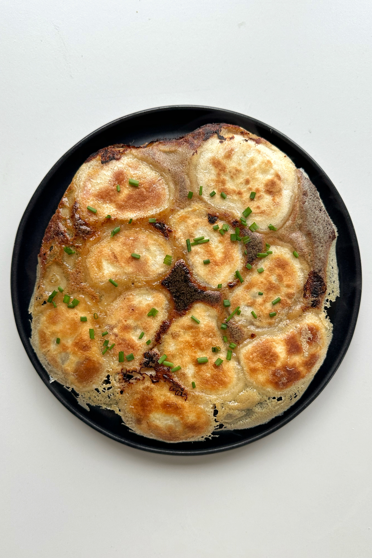 Crispy skirt dumplings on black plate topped with chives.