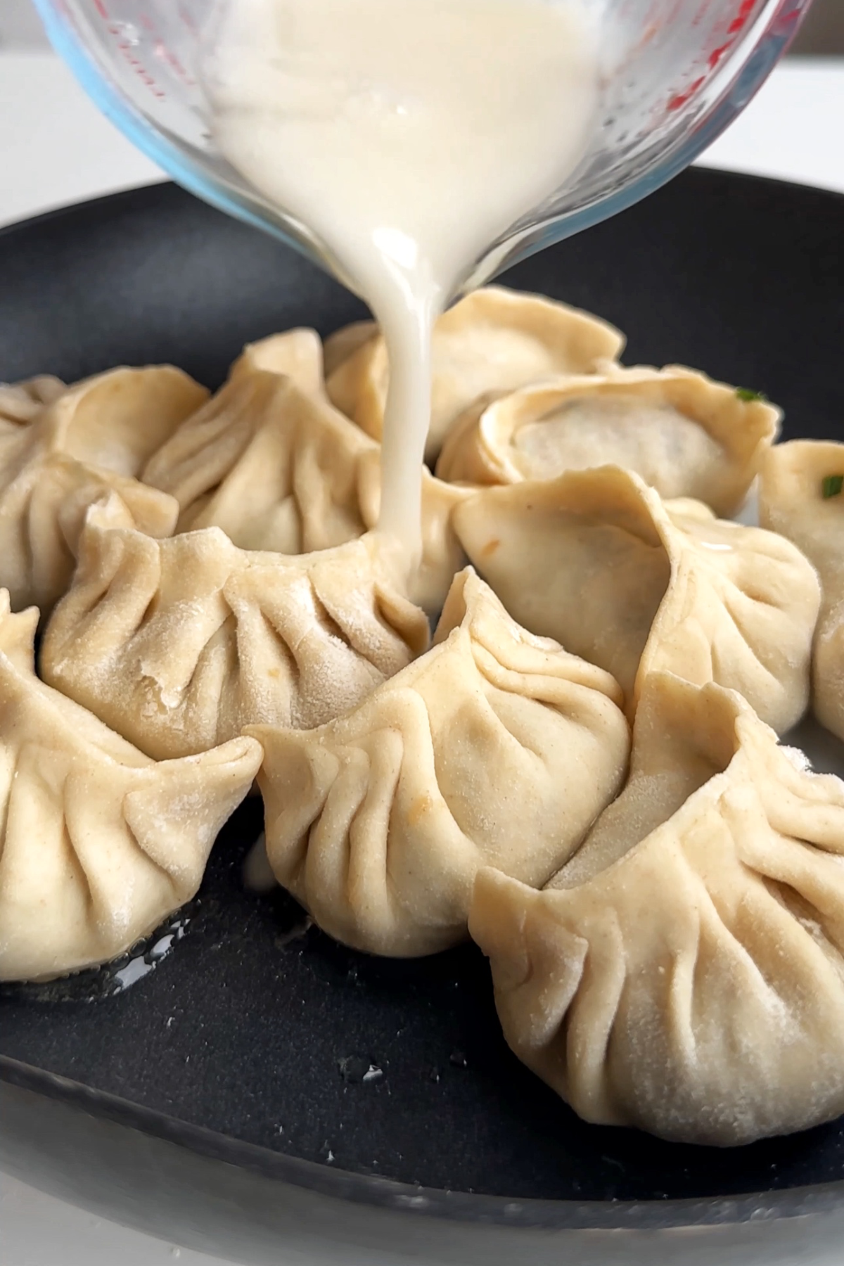 Pouring a cornstarch slurry into a non-stick frying pan full of dumplings.