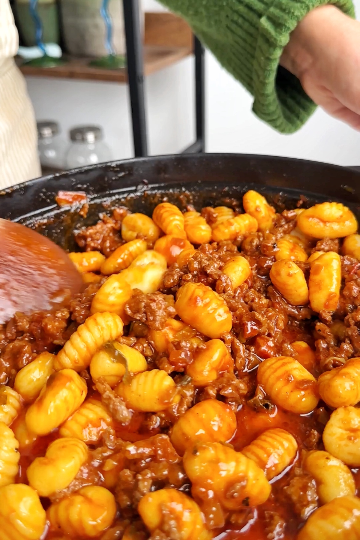 Stirring gnocchi into gochujang ragu in black pan.