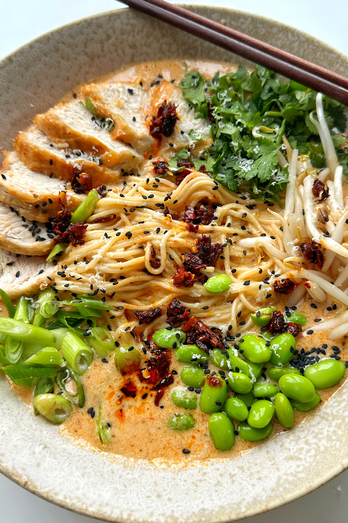 Close up of marry me chicken ramen topped with chicken, coriander, edamame, spring onions, and beansprouts.