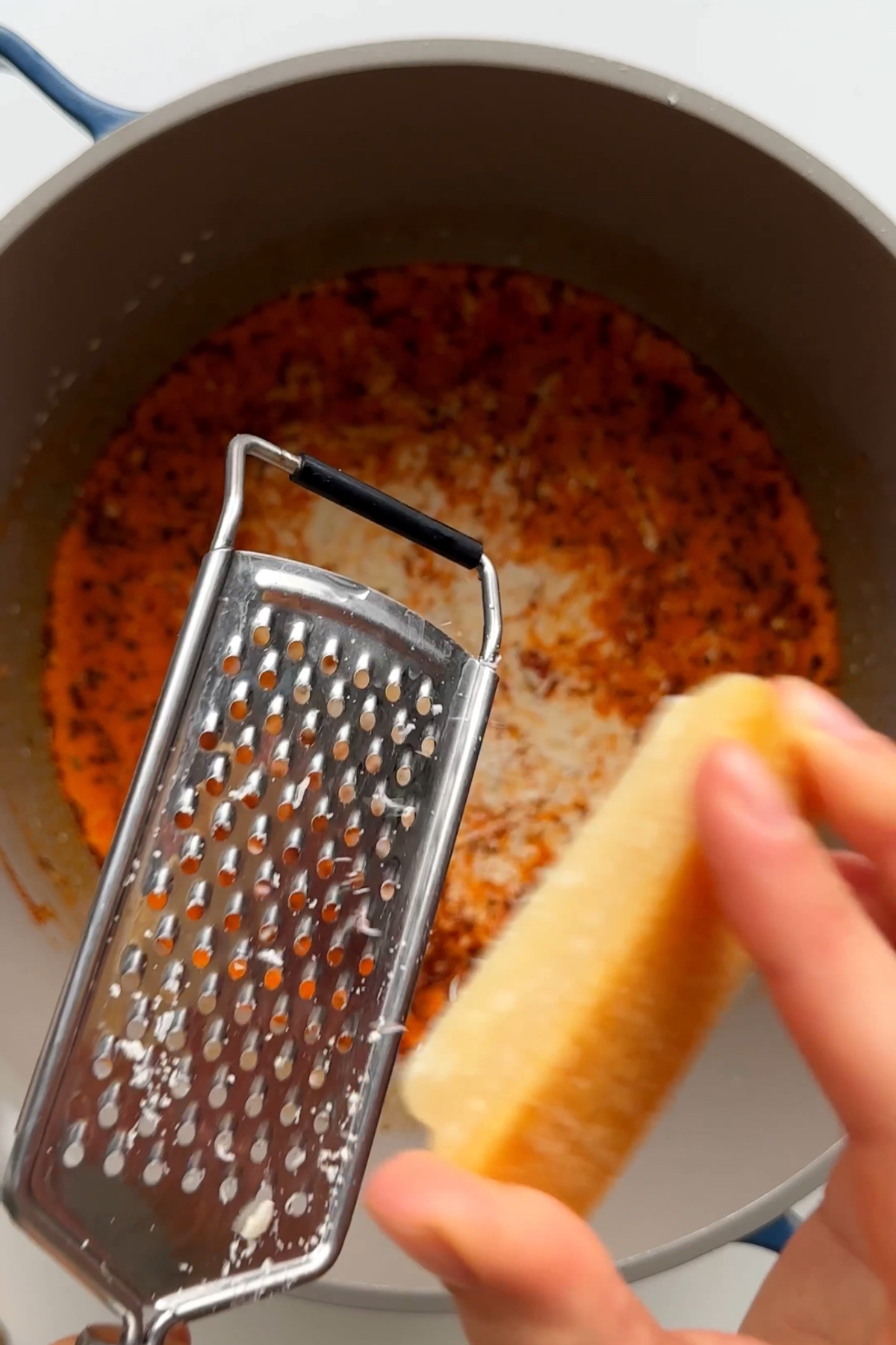 Grating parmesan into a saucepan of marry me chicken sauce.