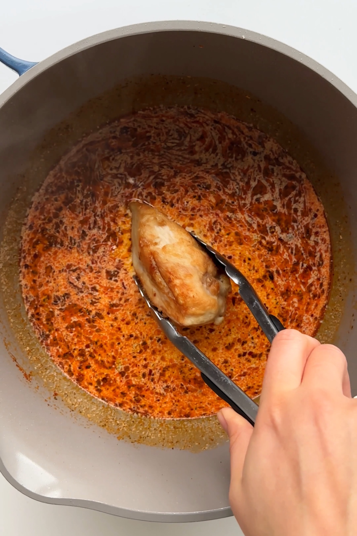 Placing a chicken breast into marry me chicken sauce.