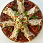 Open ended chipotle pork dumplings on a plate on a bed of tomato bean stew with avocado crush on top.