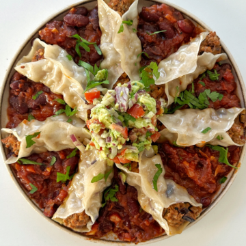 Open ended chipotle pork dumplings on a plate on a bed of tomato bean stew with avocado crush on top.
