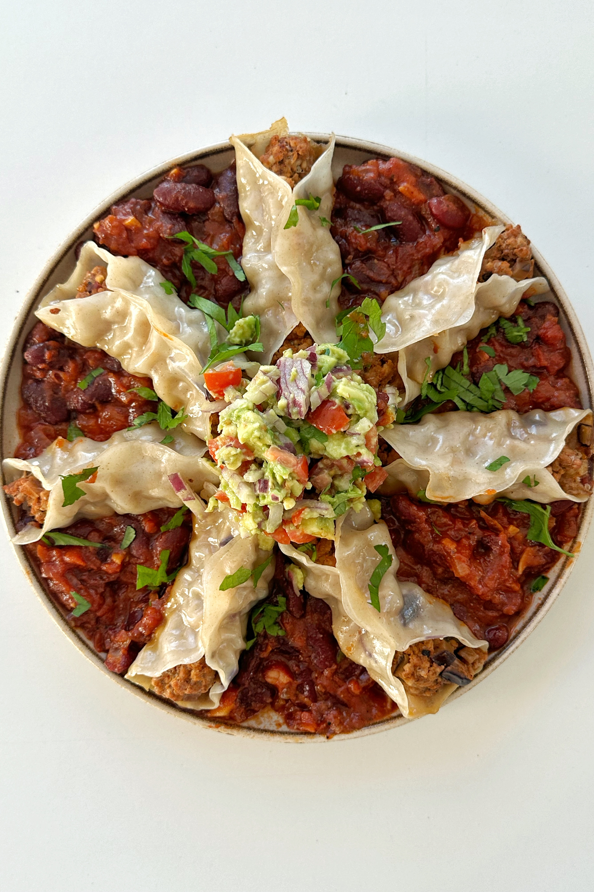 Open ended chipotle pork dumplings on a plate on a bed of tomato bean stew with avocado crush on top.