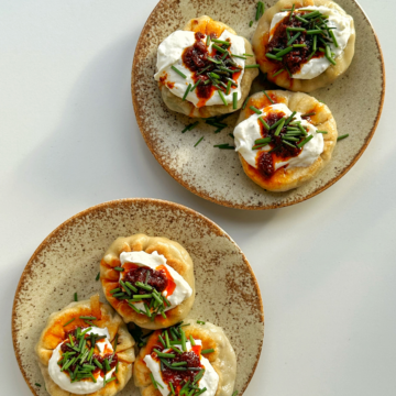 Two plates of beef spinach dumplings topped with whipped ricotta and chives.