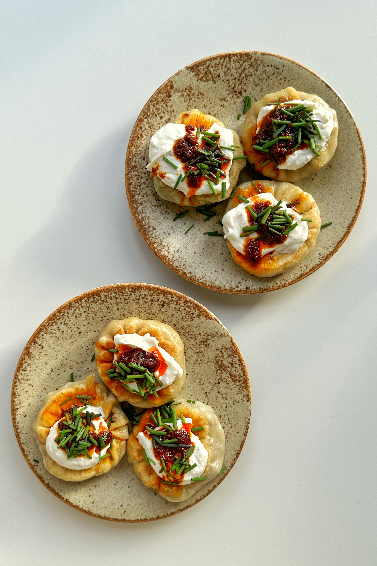 Two plates of beef spinach dumplings topped with whipped ricotta and chives.