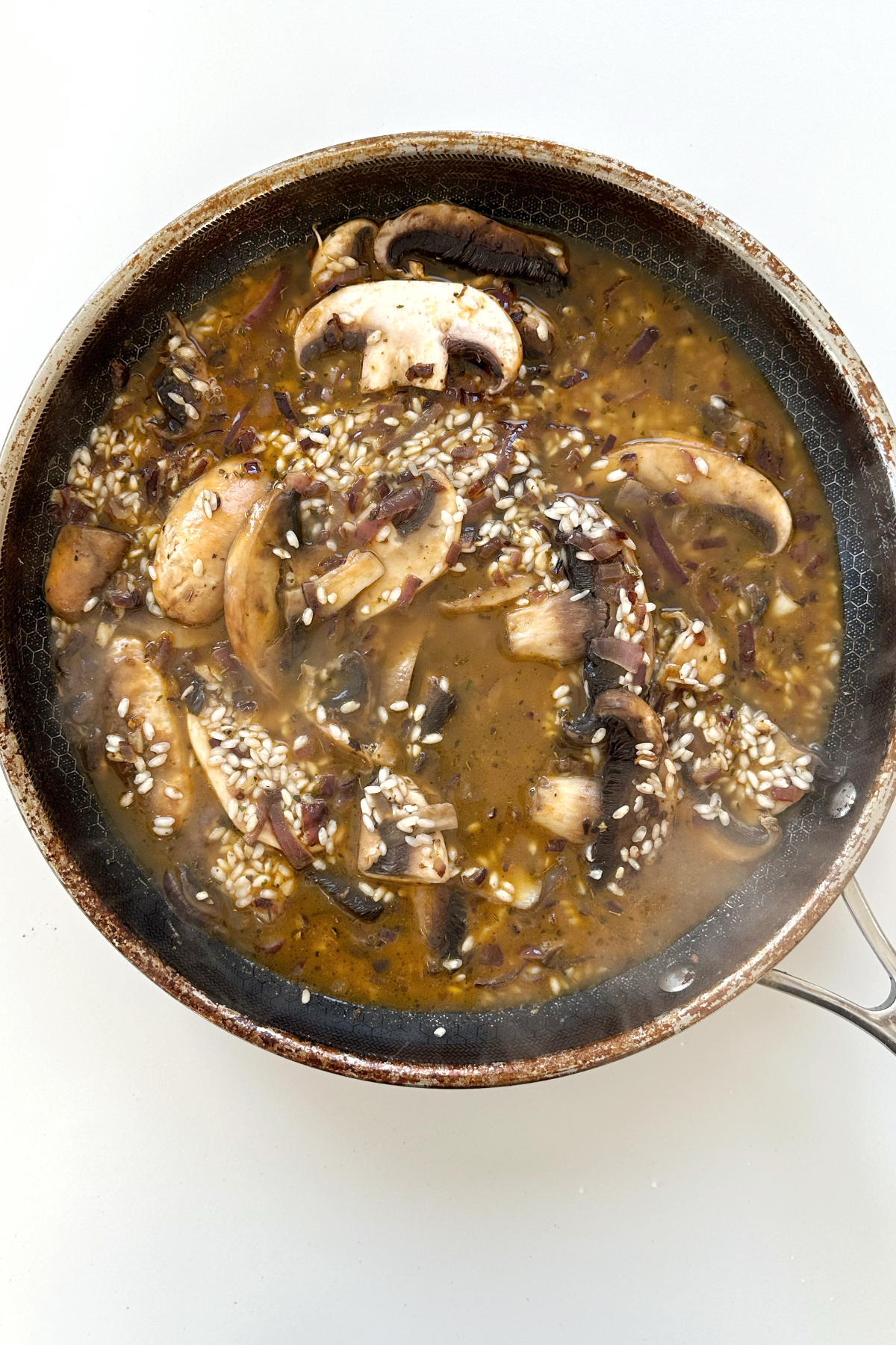 Adding stock into a black pan filled with risotto rice, mushrooms, onions, and garlic.