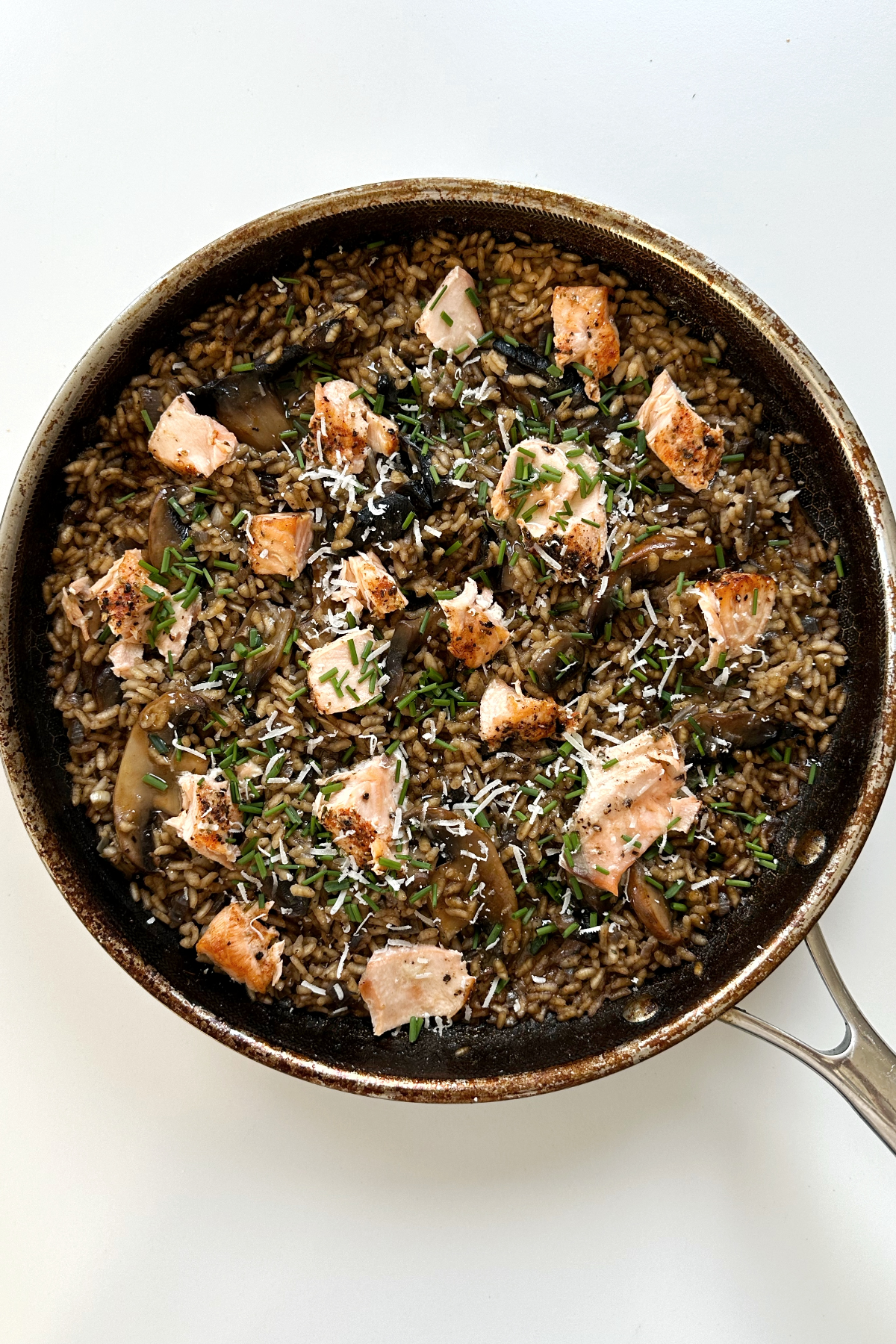 Salmon and mushroom risotto in black pan topped with parmesan cheese and chopped chives.