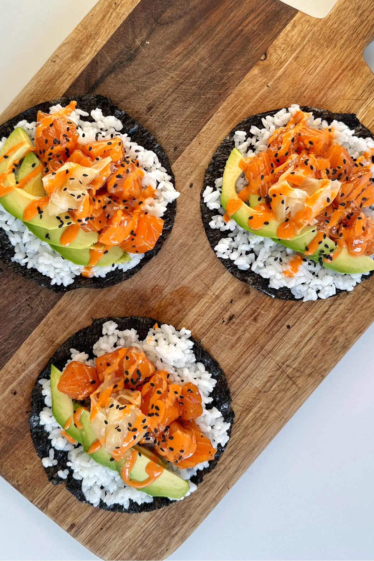 Three sushi tacos topped with salmon, avocado, and sriracha mayonnaise.