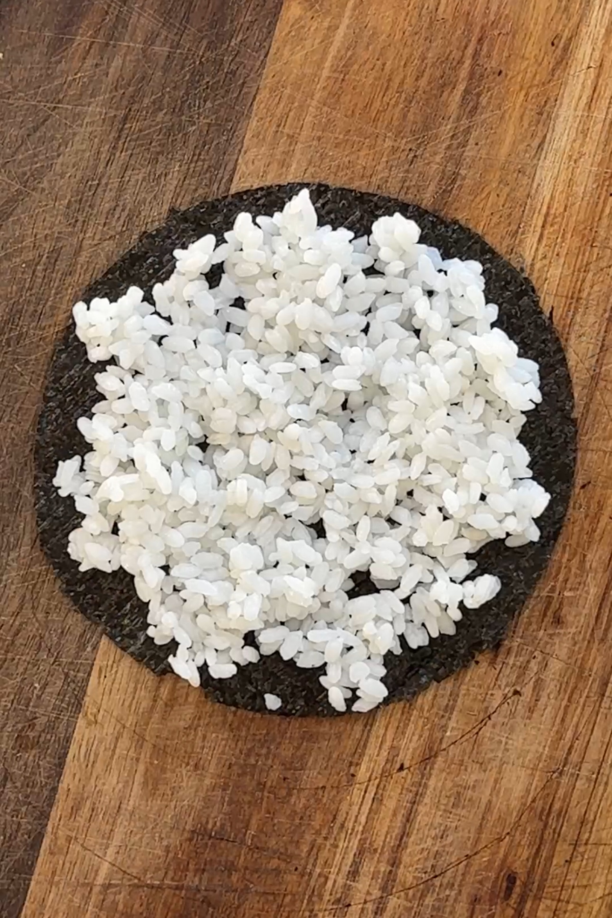 Round nori sheet on chopping board topped with sushi rice.