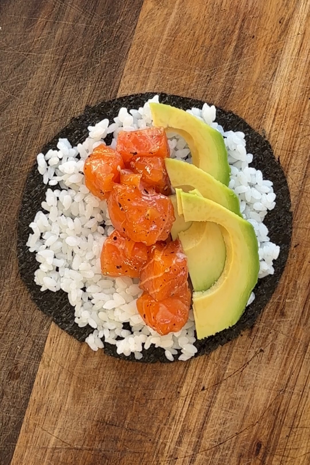 Round nori sheet topped with sushi rice, avocado slices and marinated salmon.