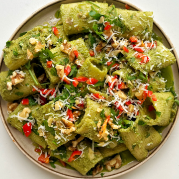 Zhoug-inspired rigatoni with walnuts, parsley, and chilli on a cream plate with a white background.