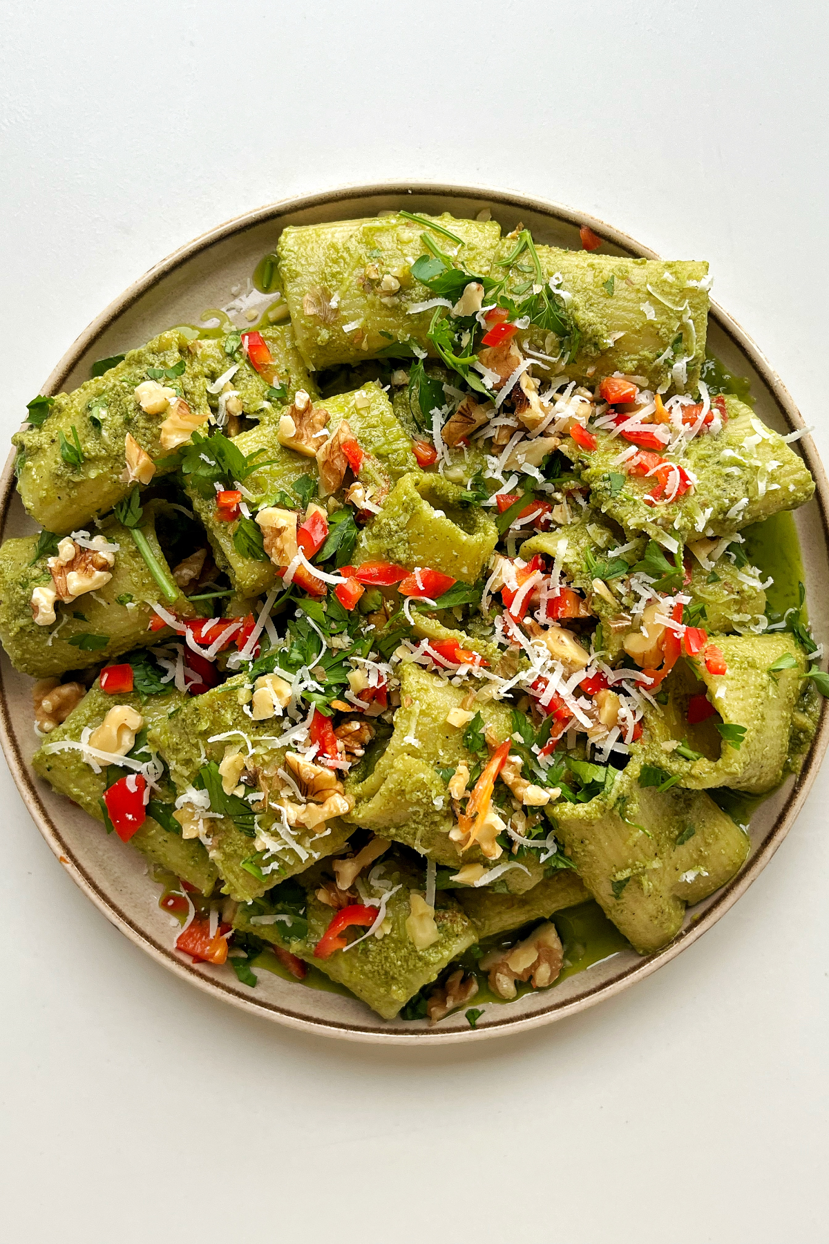 Zhoug-inspired rigatoni with walnuts, parsley, and chilli on a cream plate with a white background. 