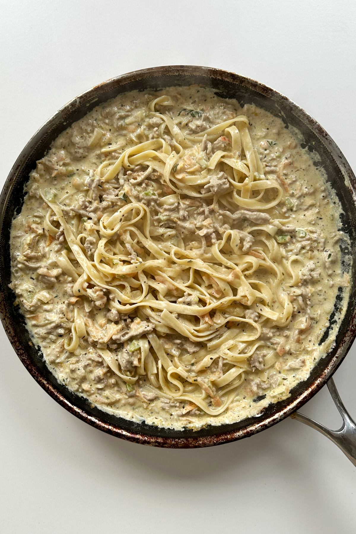 White ragu cooking in a black frying pan on white background.