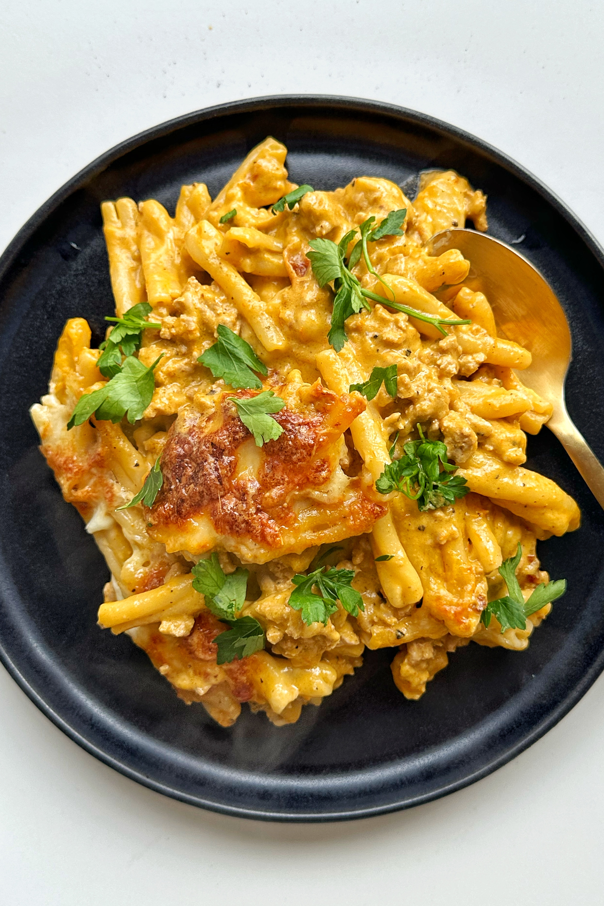 Black plate with creamy tomato pasta bake on top, topped with parsley.