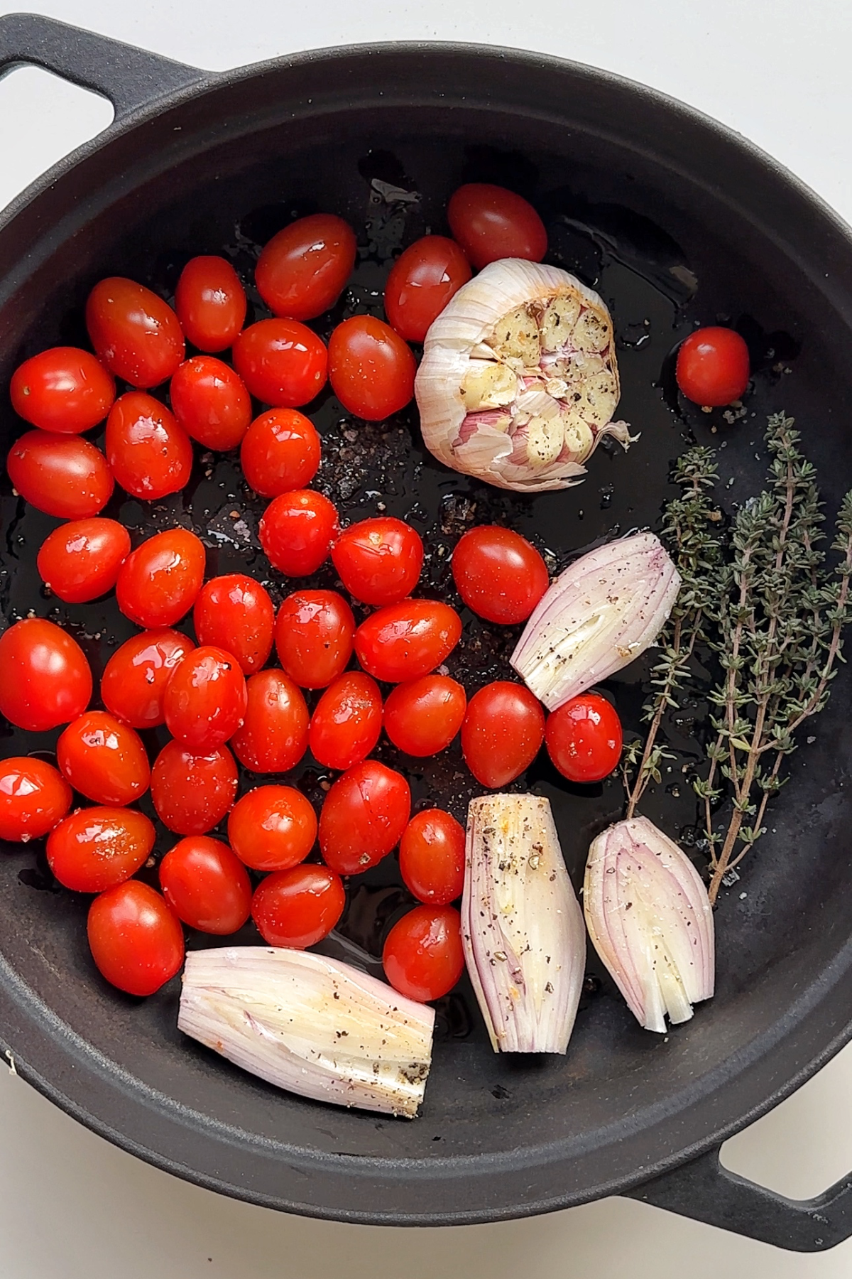 Black baking dish with tomatoes, shallots, garlic, and thyme.