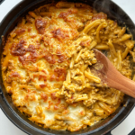 Black oven proof dish filled with baked pasta with a wooden spoon off the side.