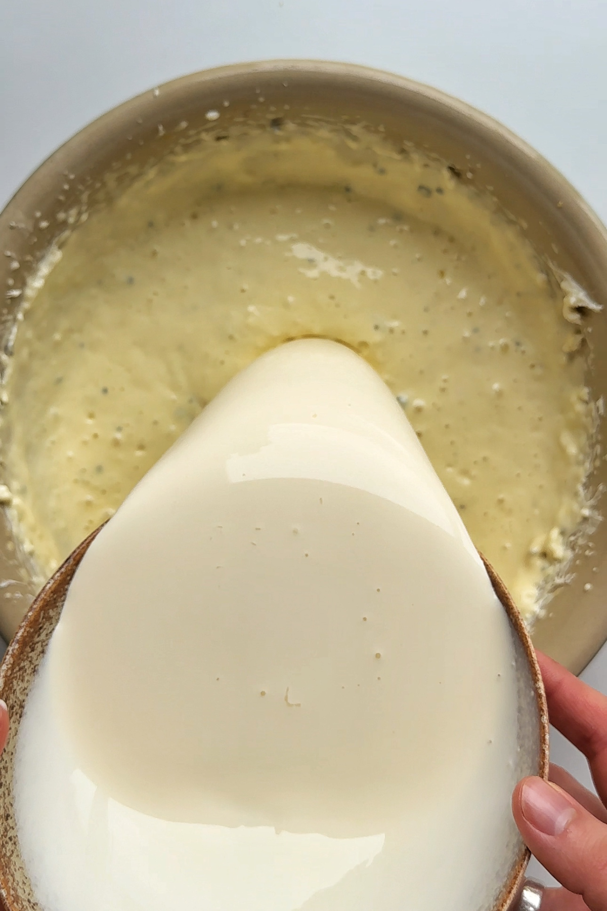 Pouring double cream into a burnt Basque savoury cheesecake mixture.