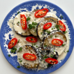 A blue plate topped with aubergine discs, red chillies, and parsley.