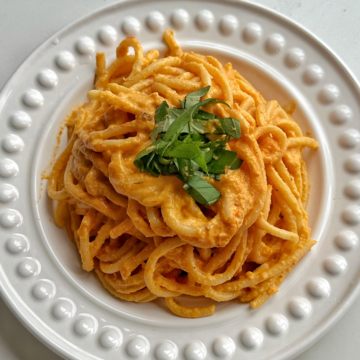 White plate topped with a creamy bucatini pasta, garnished with basil.