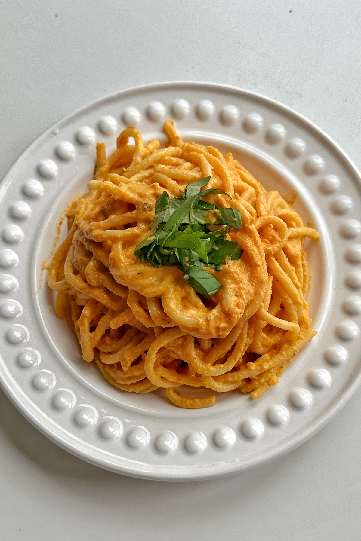 White plate topped with a creamy bucatini pasta, garnished with basil. 