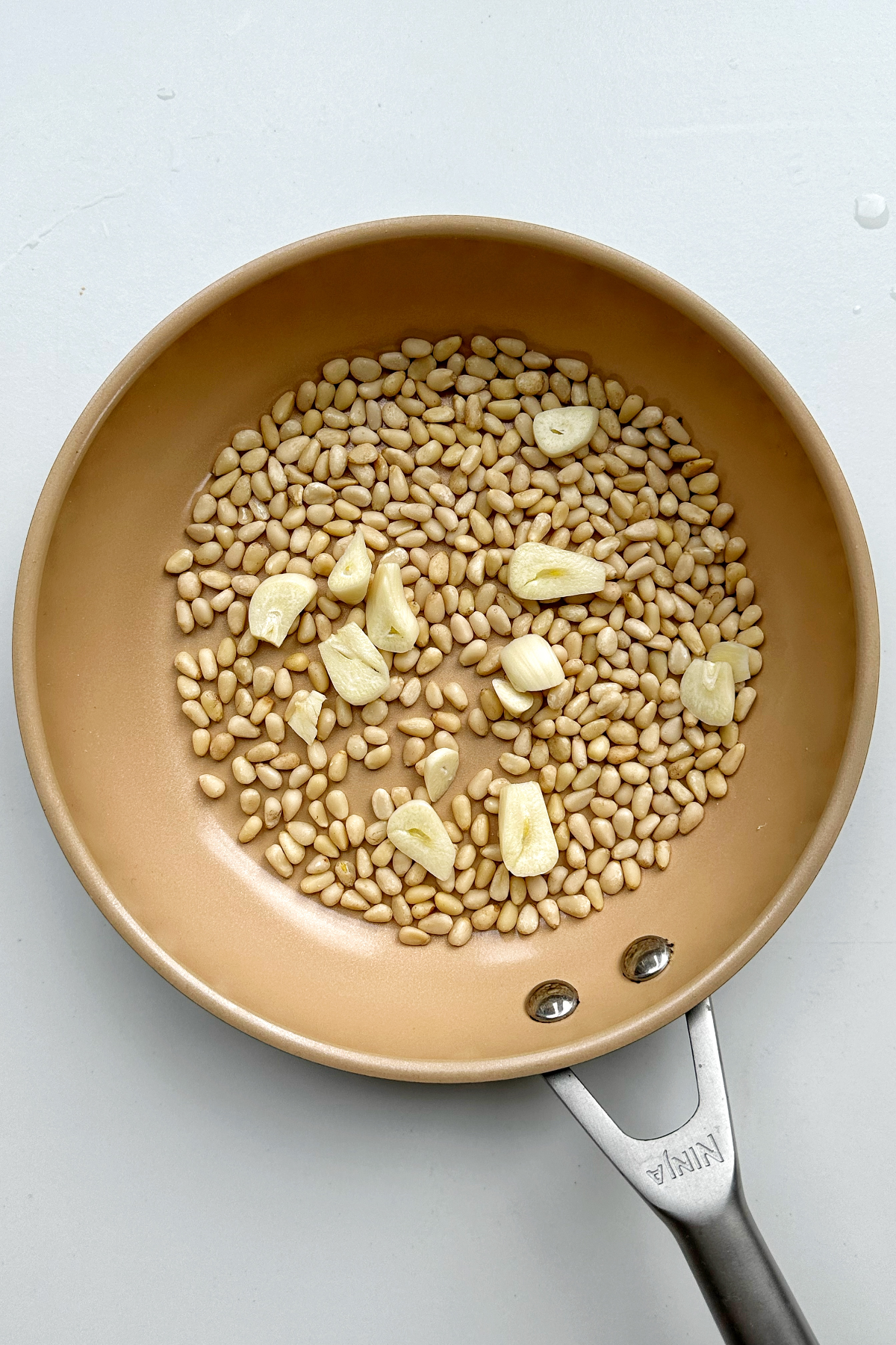 Toasting pine nuts and garlic in a frying pan.