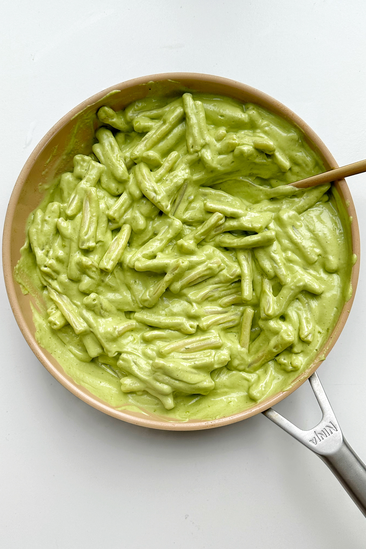 Avocado pesto combined with pasta in a frying pan.