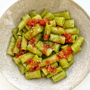 Green cilantro pasta topped with a paprika tomato dressing in a cream bowl on a white surface.